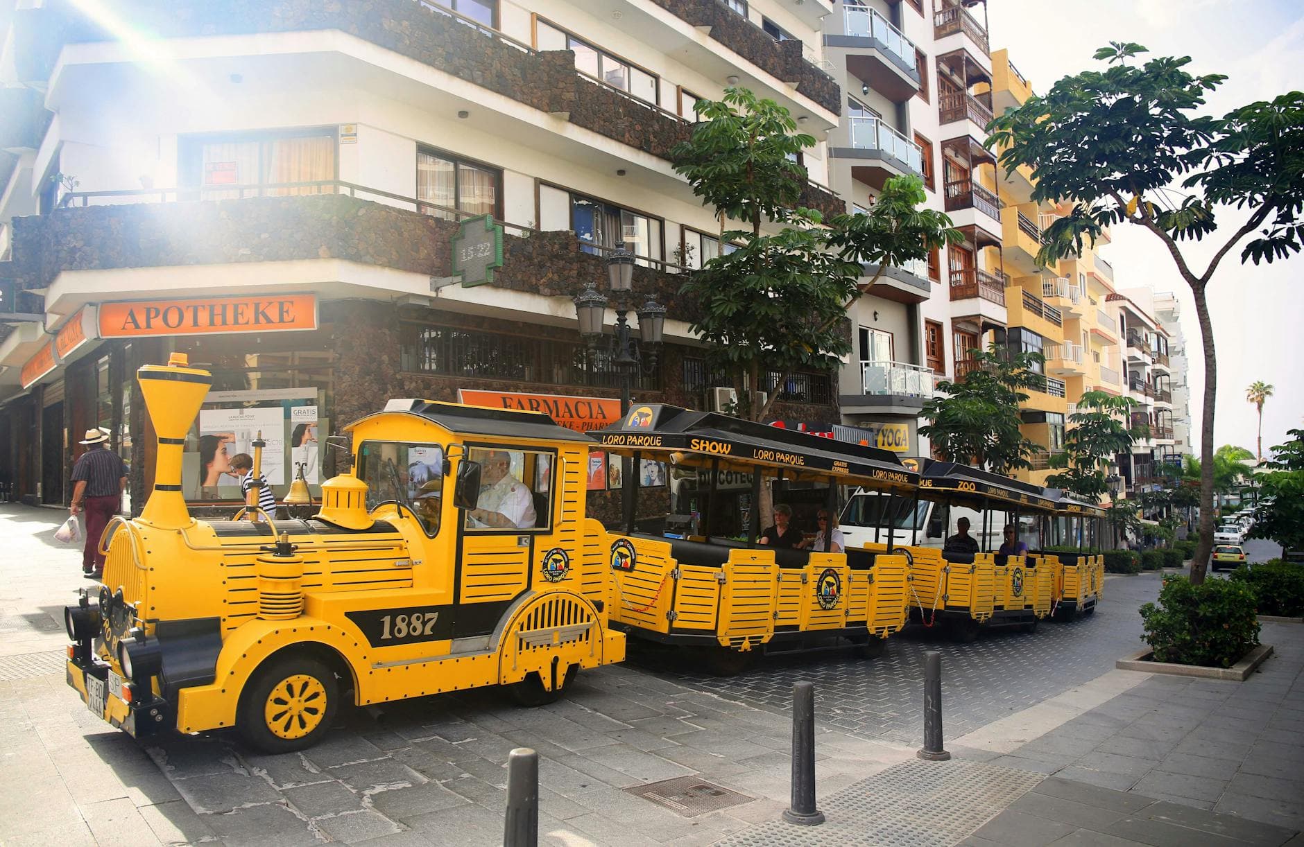 Vibrant yellow tourist train passing by urban architectural buildings in Santa Cruz de Tenerife.
