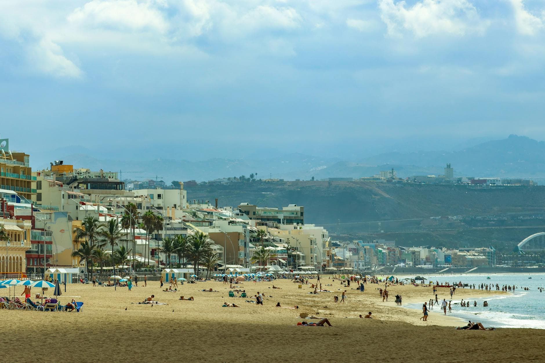Vibrant beach scene in Las Palmas, Gran Canaria, showcasing sunny coastline with people and architecture.