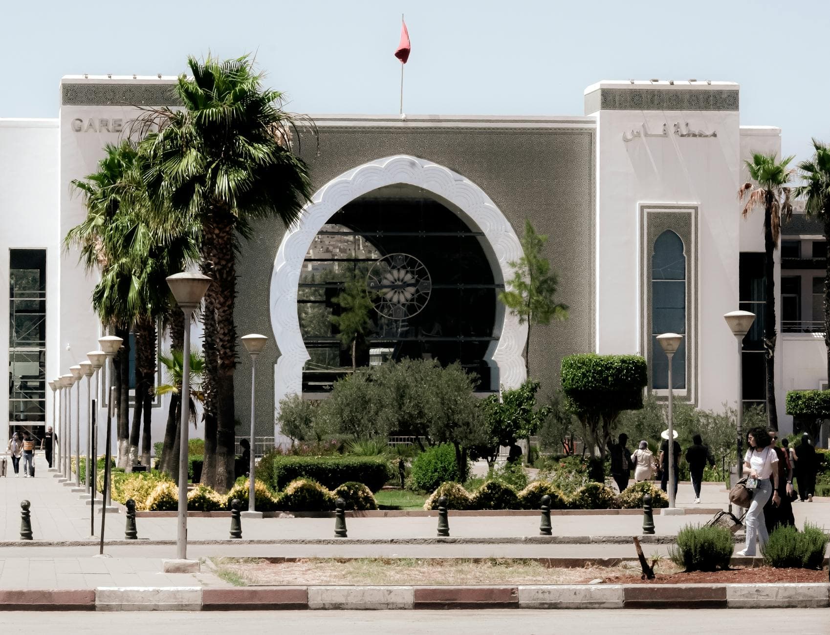 A beautifully ornamented train station entrance in Fez, Morocco, with palm trees and cultural architecture.